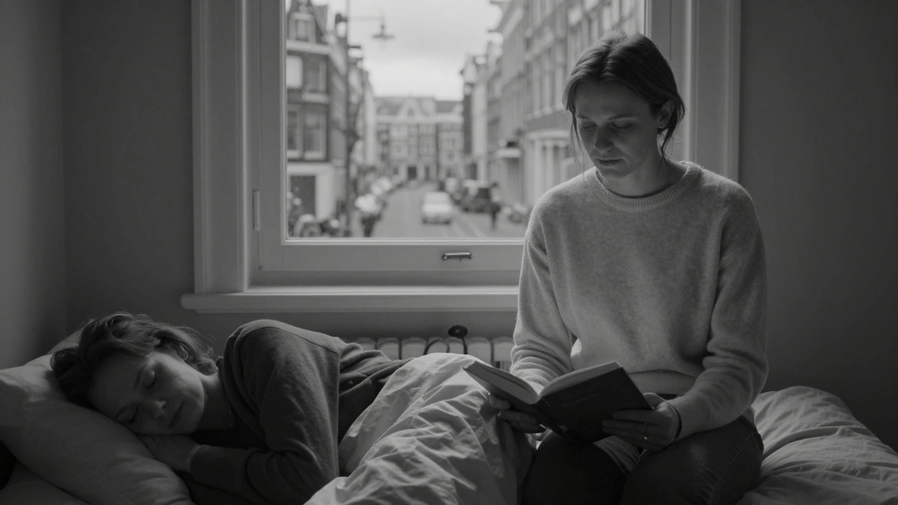 A woman reads a book beside a sleeping client in a quiet room, soft light falling on her hands and the page.